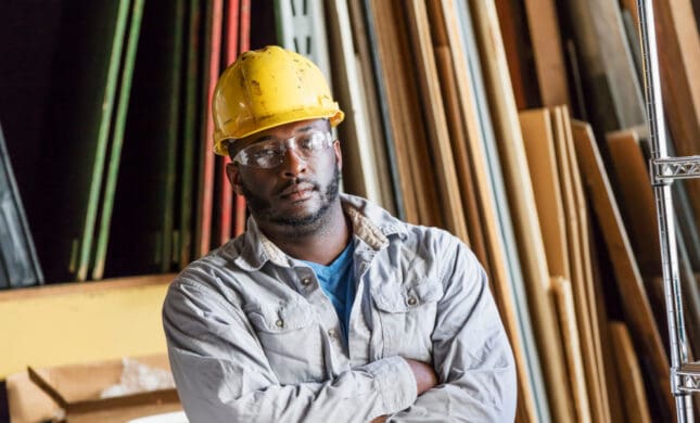 Serious construction worker in hard hat amid wooden planks, considering workplace injury claim