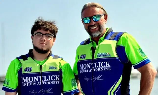 Two smiling individuals wearing bright green and blue cycling jerseys that say "Montlick Injury Attorneys" stand side-by-side outdoors on a sunny day, with sunglasses reflecting the blue sky.