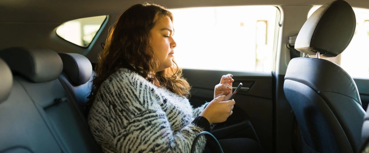 Young woman interacting with her phone while sitting in the back seat of a rideshare vehicle