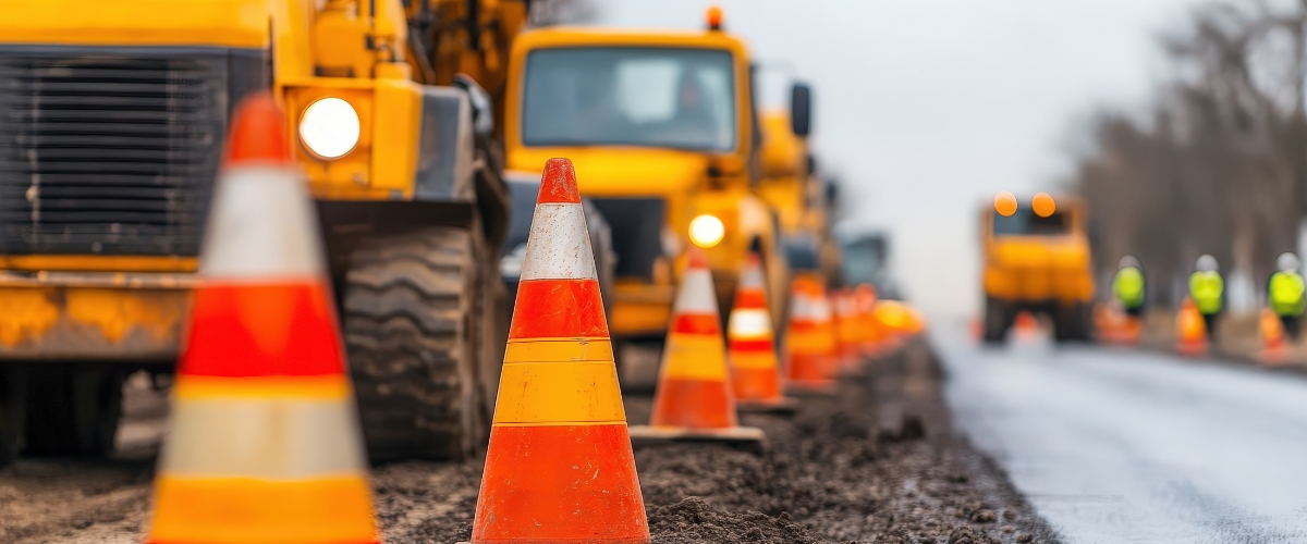 Heavy duty trucks and yellow cones alongside a highway construction site